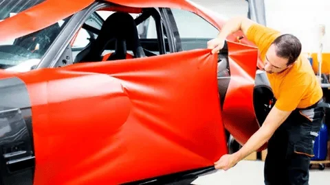 A Man Wrapping Car Door With Red Wrap